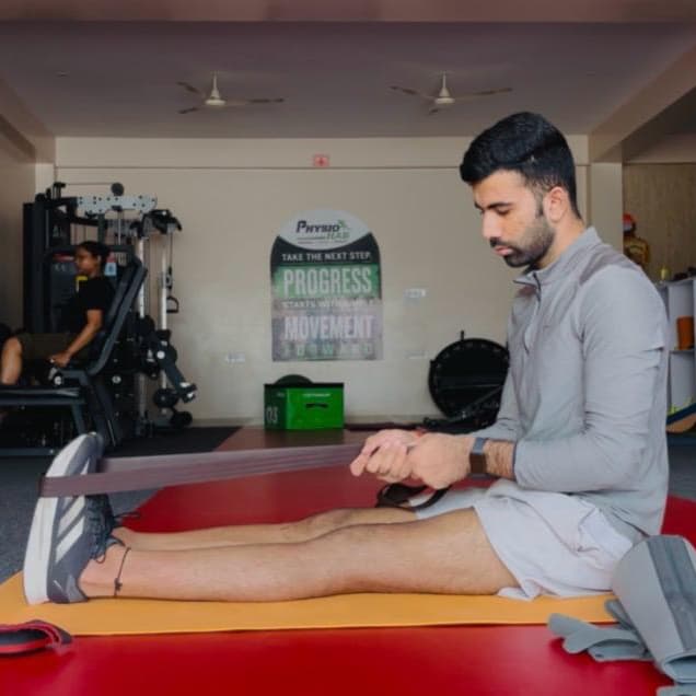ACL PhysioHab therapist assisting a patient with a resistance-band hamstring stretch during a rehab session