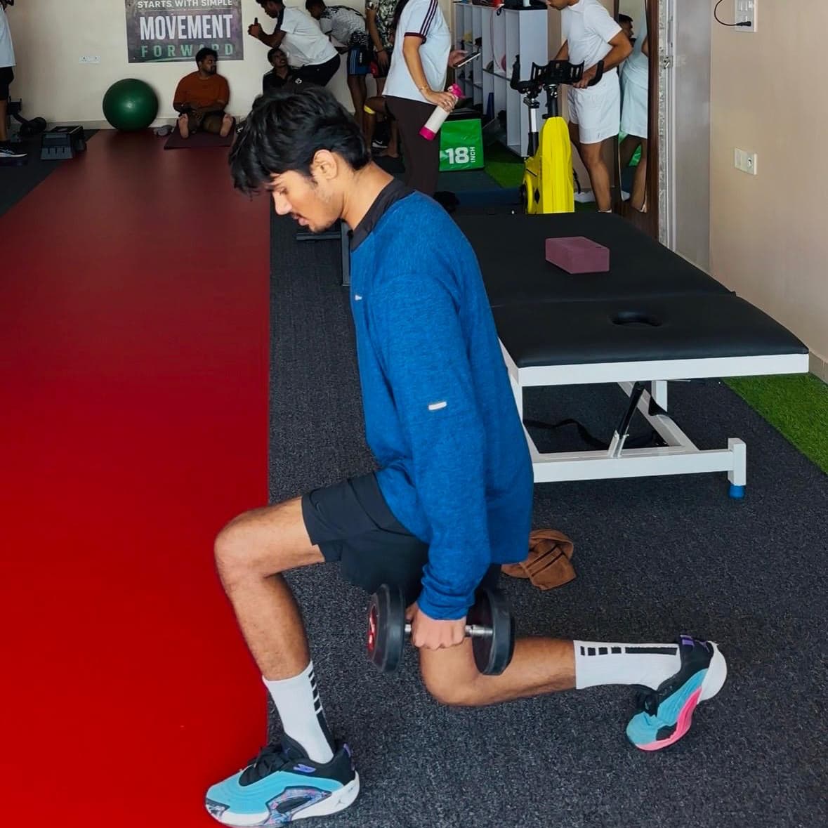 Patient performing a weighted reverse lunge with dumbbells near the treatment table at ACL PhysioHab