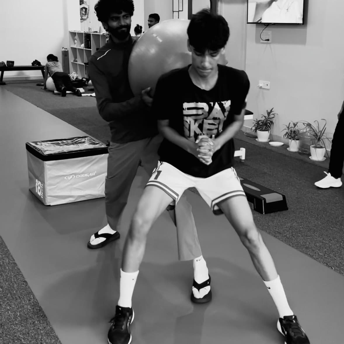 Physiotherapist supporting a young athlete through a single-leg balance drill using a stability ball for perturbation training