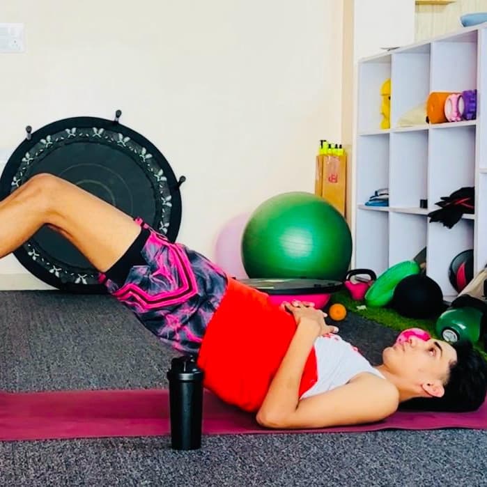 Patient performing a glute bridge exercise on a mat, surrounded by stability balls and rehab equipment