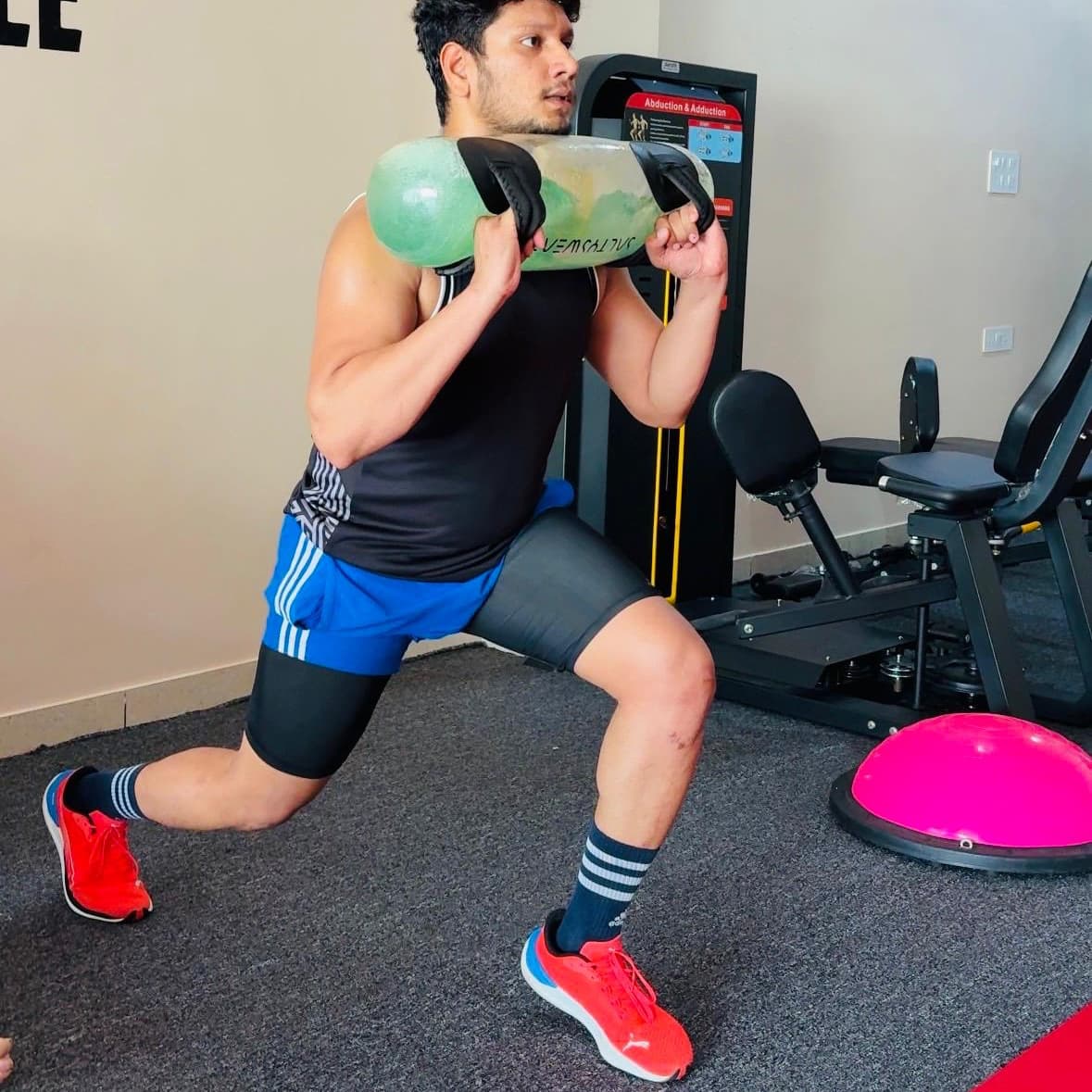Patient performing a weighted walking lunge with a sandbag across the shoulders near the leg press machine
