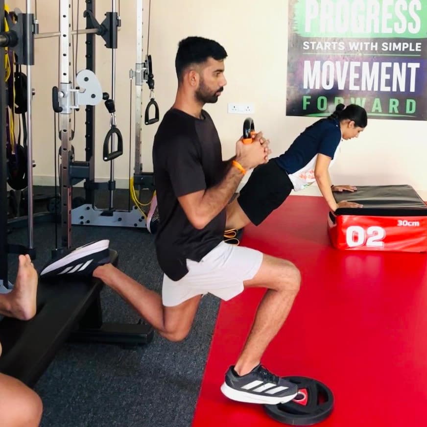 Two patients performing rear-foot-elevated split squats and a plank hold side by side on the clinic floor