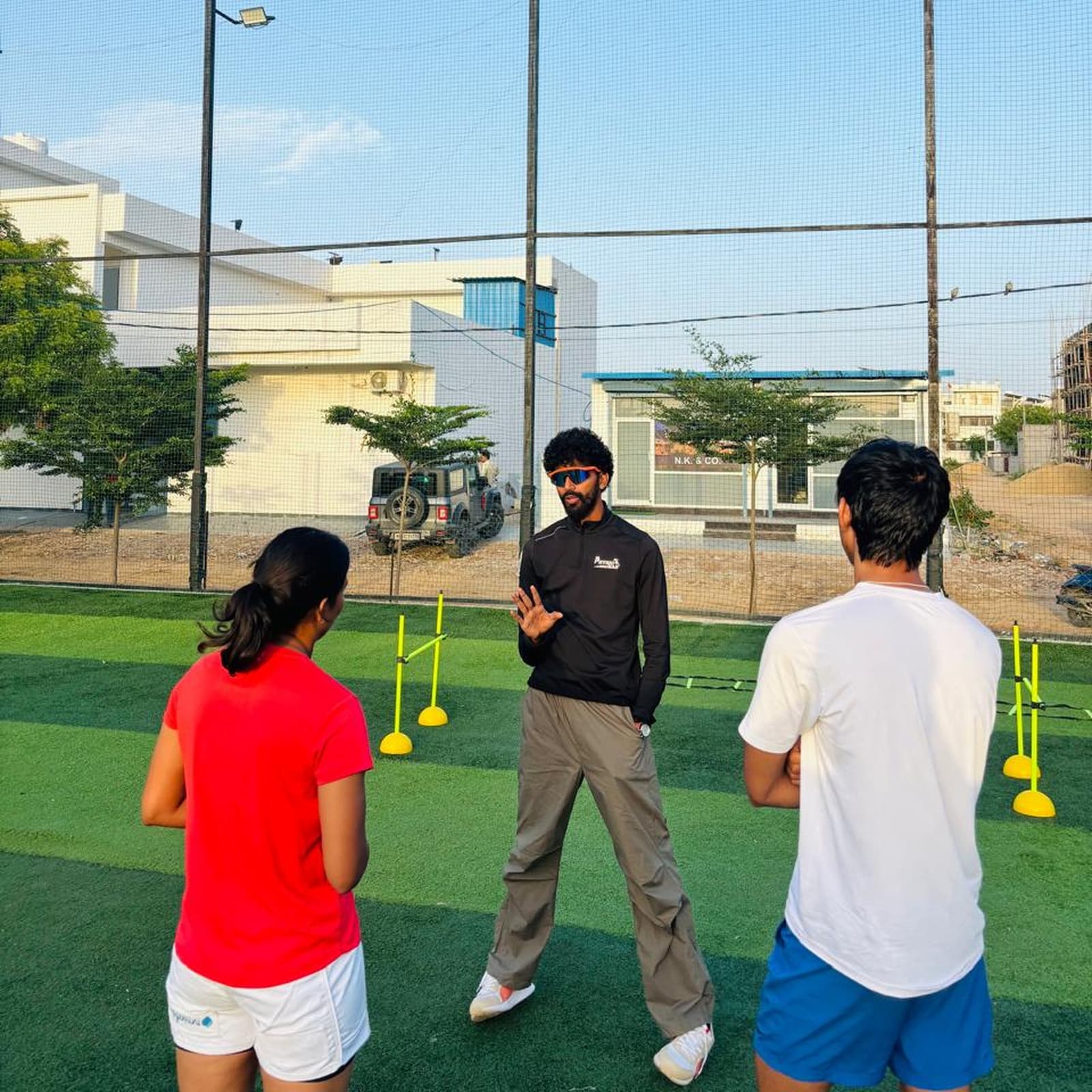 ACL PhysioHab coach briefing two athletes before an outdoor agility drill set up with cones and mini hurdles