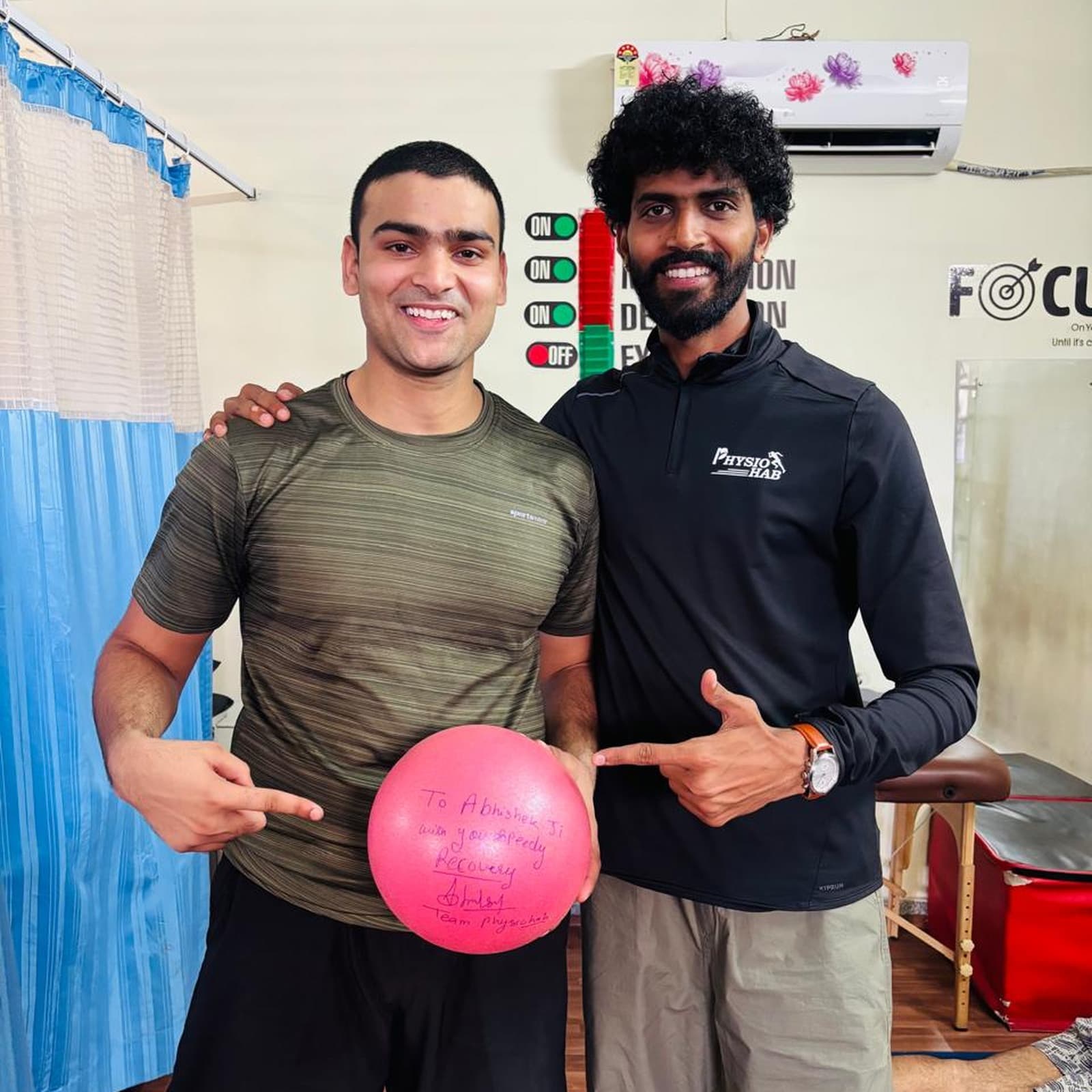 Recovered patient posing with his ACL PhysioHab physiotherapist, holding a ball signed with a speedy-recovery message