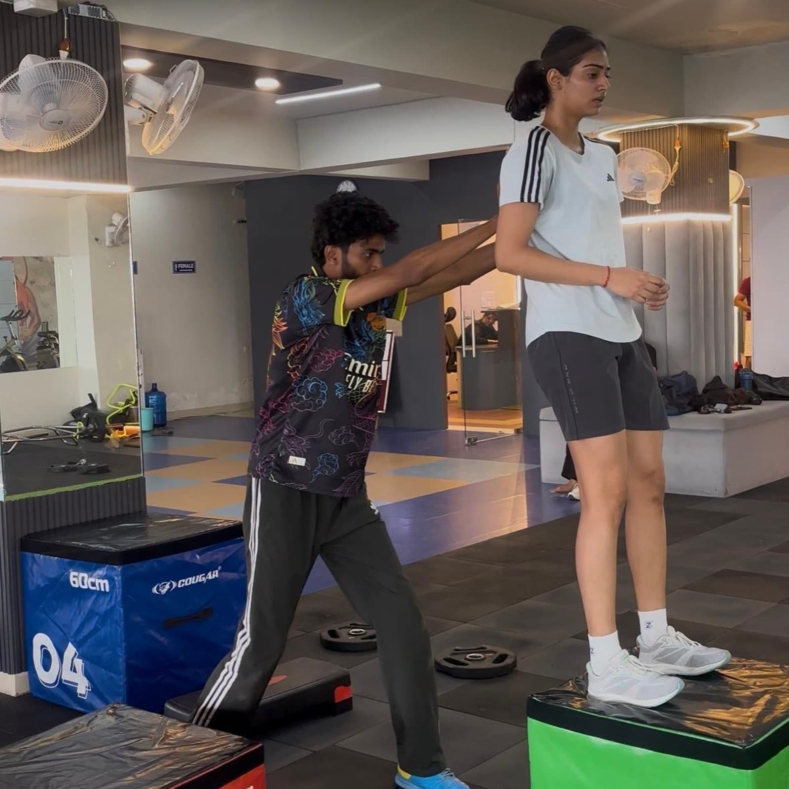 Physiotherapist spotting a patient's balance as she steps down from a plyo box during a training session